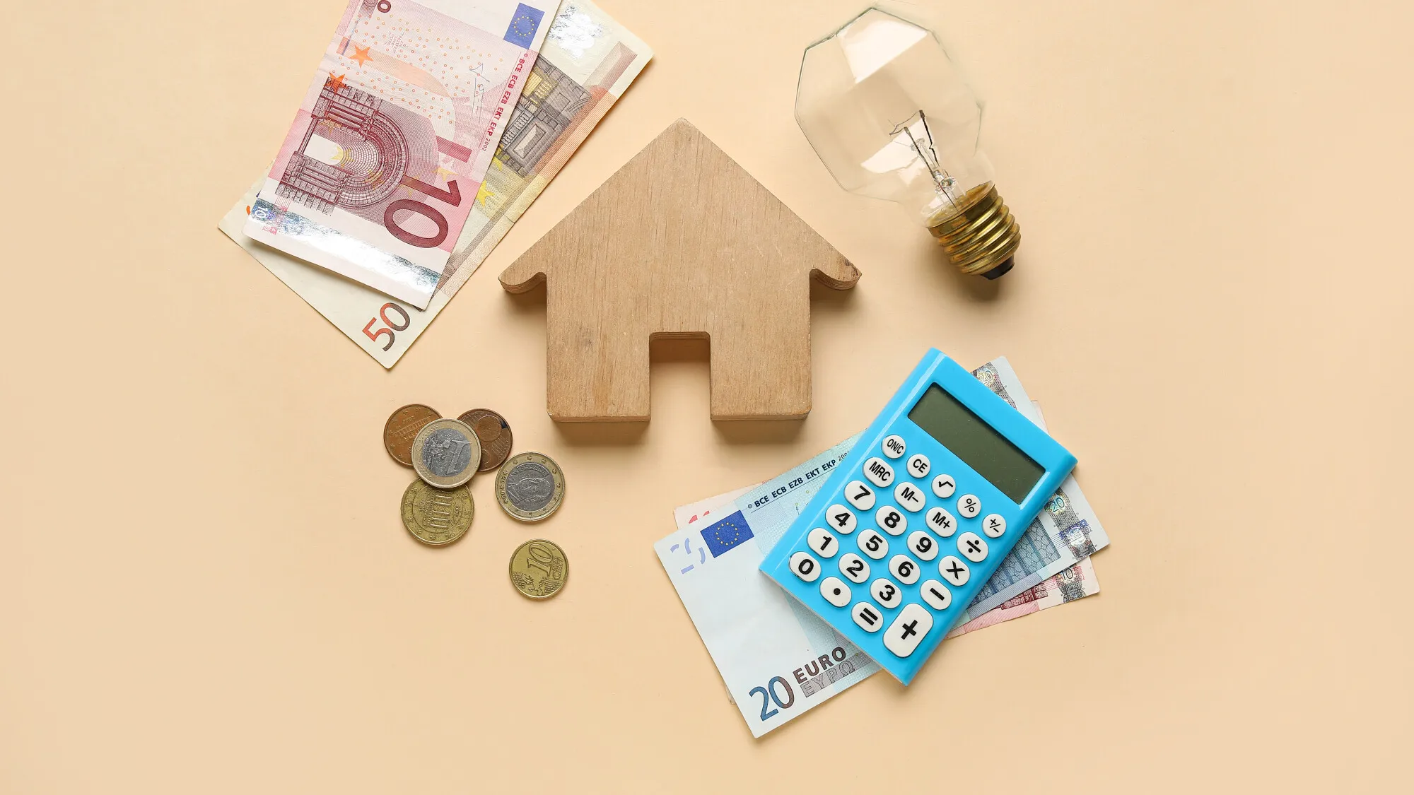 Mise en scène avec une petite maison en bois, des billets de banque, des pièces de monnaie, une calculatrice, et une ampoule symbolisant les idées et la gestion financière.